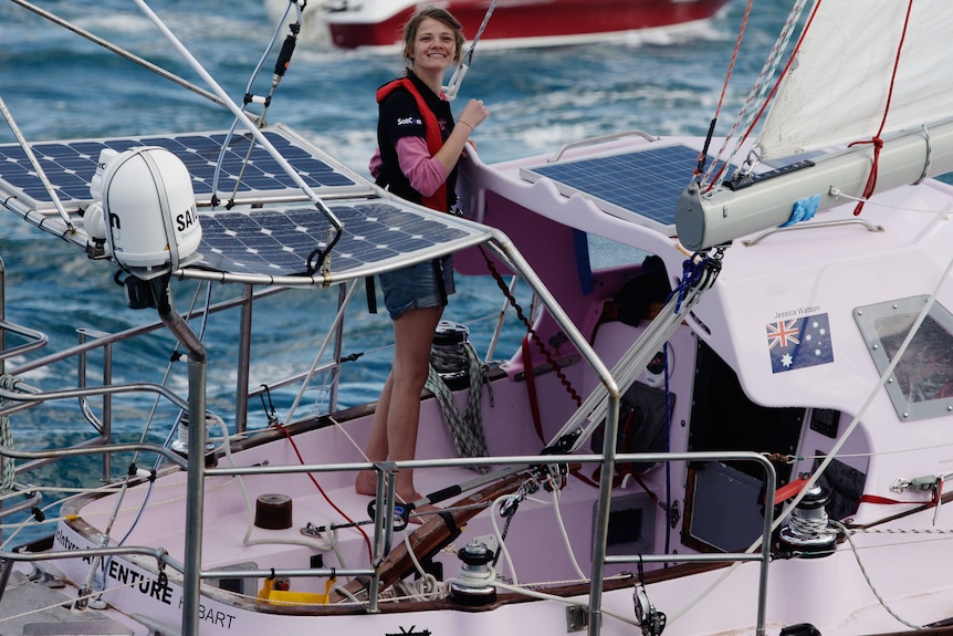 Jessica smiling, standing on her pink sail boat, water behind.