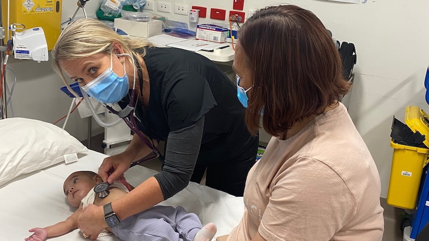 A doctor treats a child in a hospital while the child's mother watches on. 