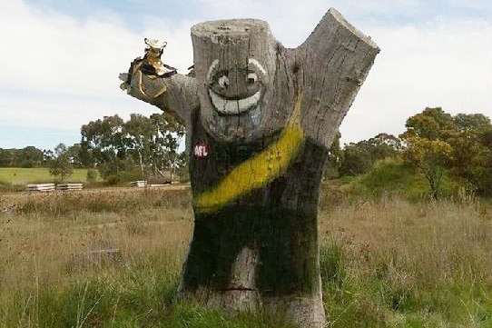 A tree stump has been decorated to look like a Richmond player who is holding a premiership cup