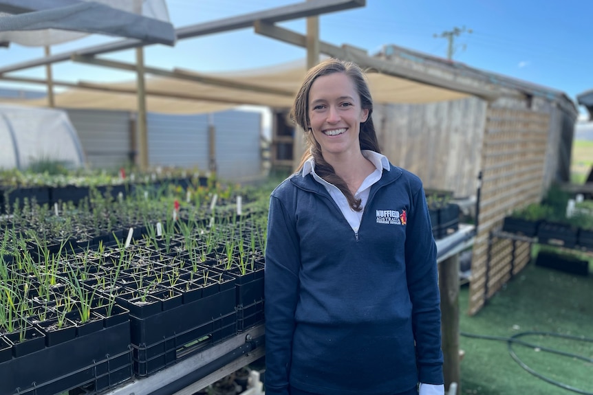 Young woman with brown hair smiles standing in front of rows of seedlings