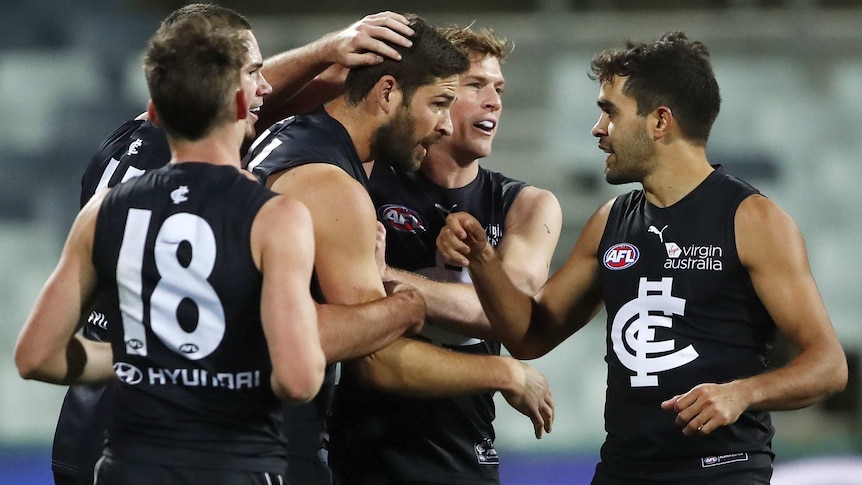 An AFL player gets patted on the head and back by teammates after his goal.