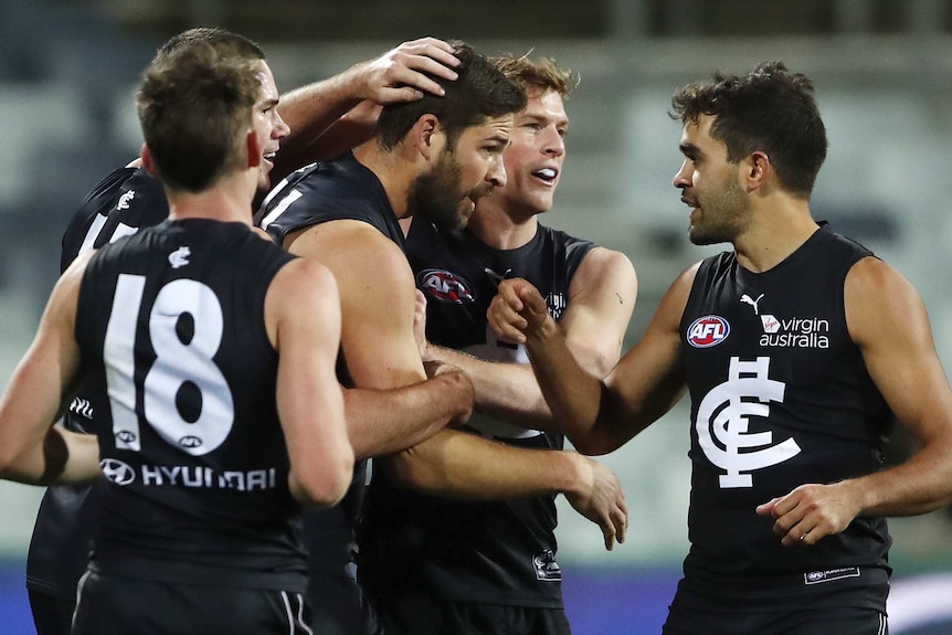 An AFL player gets patted on the head and back by teammates after his goal.