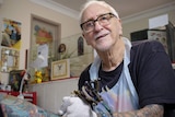 Tattoo artist Les Bowen looks up while working on a man's tattooed arm in his studio