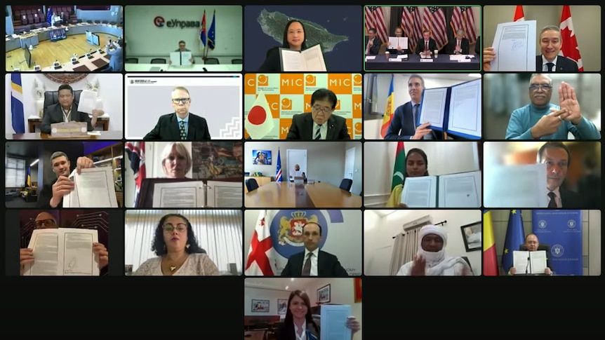 A screenshot of more than a dozen people in separate locations holding up pieces of paper during an online video conference.