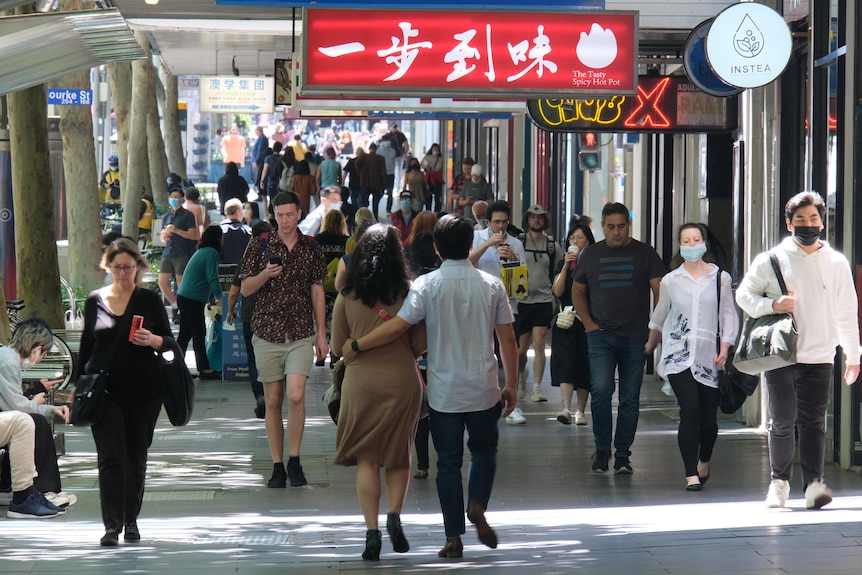 A man and woman walk closely down a Melbourne footpath, surrounded by other people