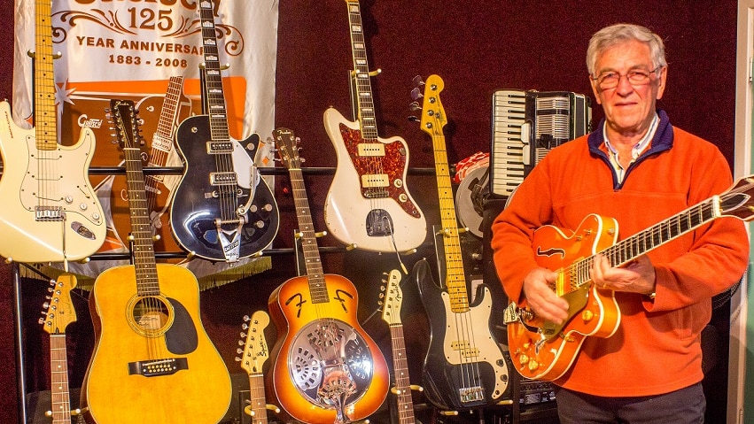 A man stands in front of guitars