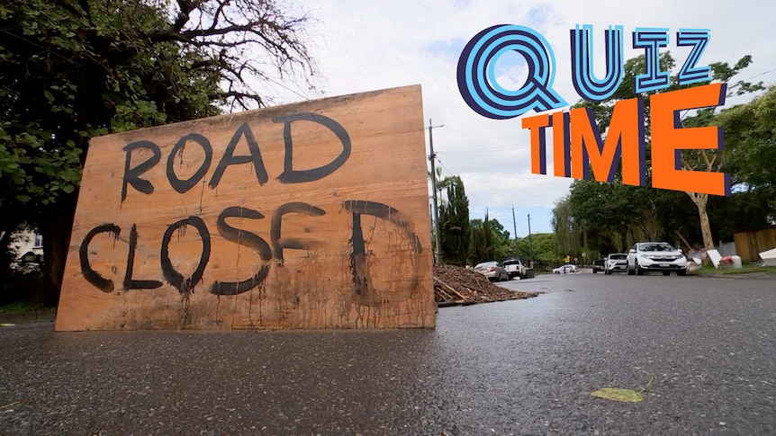 A sign on a road saying "Road Closed", with flood debris behind it.