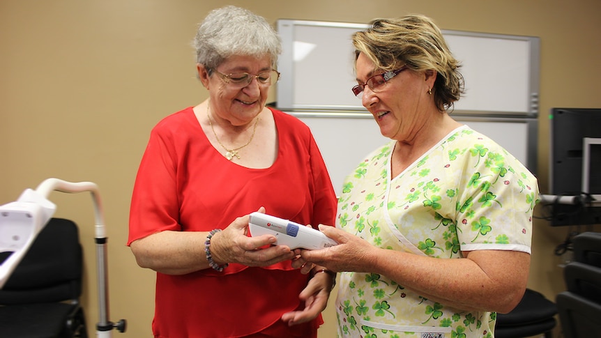 Catherine Iseppi hands over the handheld device to clinical nurse Elizabeth Ratcliffe