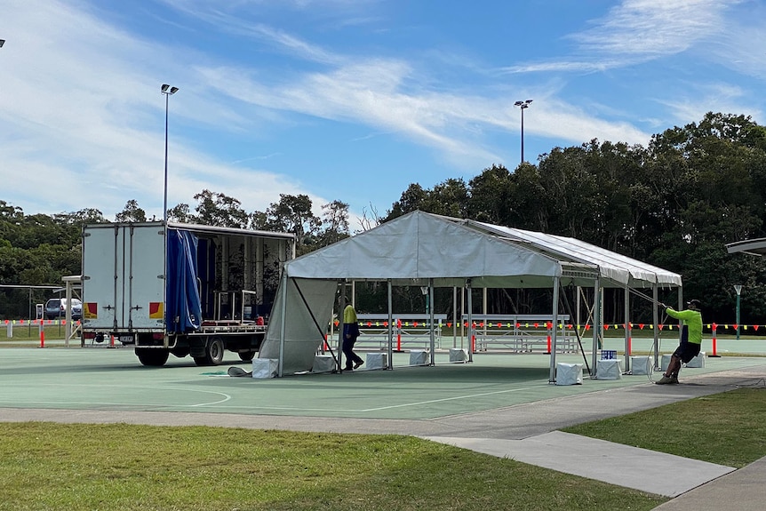 Men set up marquees on a netball court for COVID-19 pop-up vaccination hub