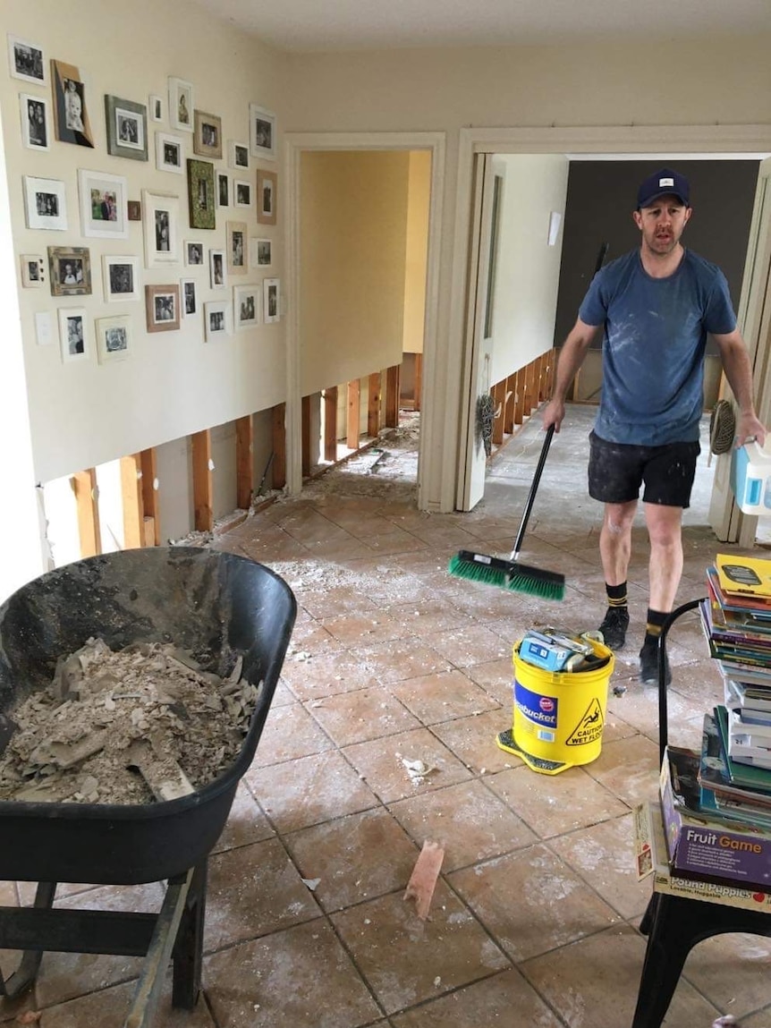 a photo of a man with a broom cleaning up in a semi-gutted home 