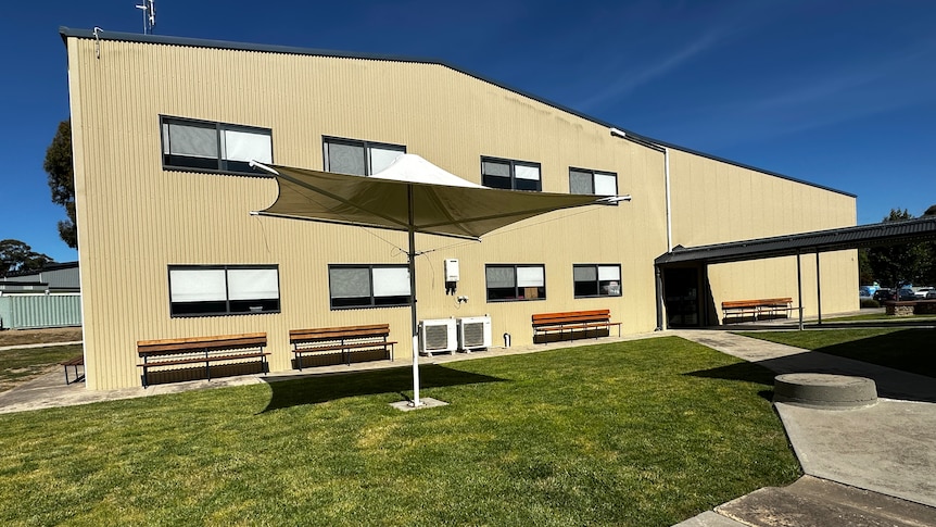 A double-storey building painted sandstone yellow, with grass and concrete at the front.