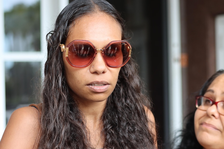 a young woman wearing sunglasses looks down outside court