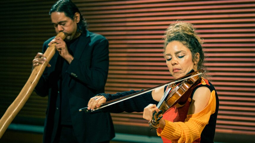 William Barton plays didgeridoo in the background, with Veronique Serret playing violin in the foreground.