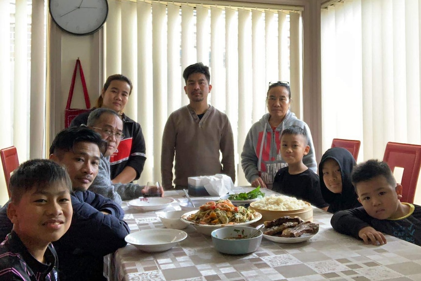 Members of a family sit and stand around a dining table