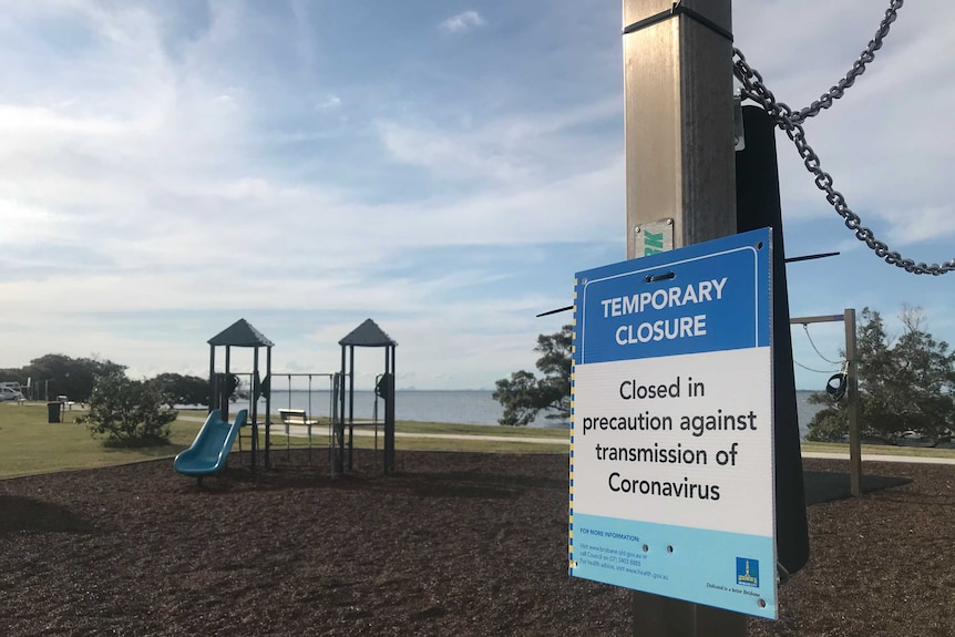 A sign that explains the closure of a playground is fixed to a set of swings which have been tied up.