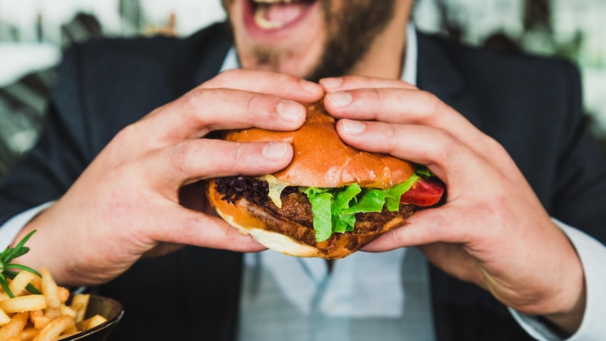 A man with a wide open mouth leans into a hamburger