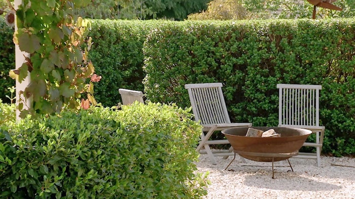 Formal garden with hedges surrounding chairs and a metal fire pit
