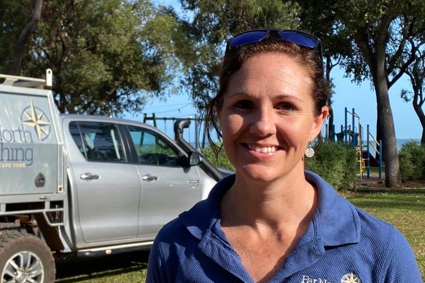 A woman wearing a purple polo shirt standing in front of a ute, looking at the camera