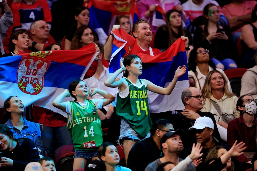 Two young basketball fans wearing Australian Opals singlets dance in the crowd.