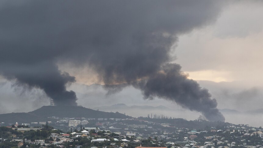 Smoke rises from two separate columns over a city dotted with low-rise homes and buildings