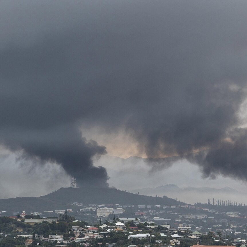 Smoke rises from two separate columns over a city dotted with low-rise homes and buildings