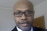 A man wearing a suit and glasses looks at the camera.
