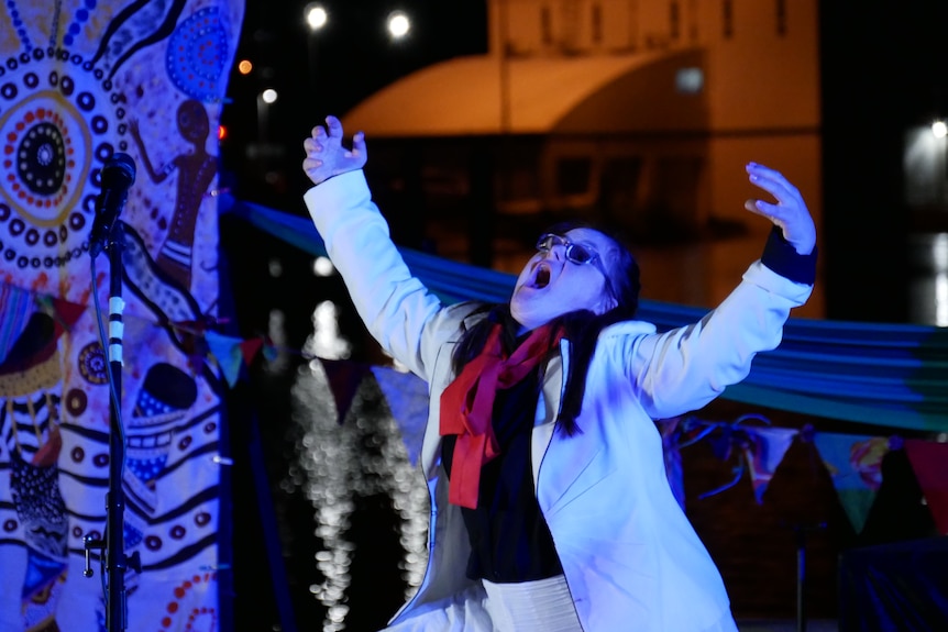 Woman in white and red costume performs on stage, under a blue light 