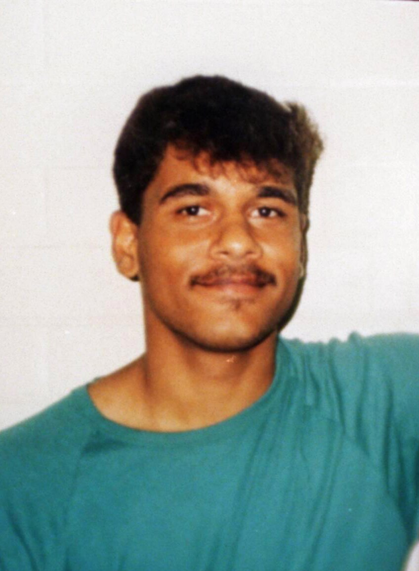 Headshot of a young man with a moustache wearing prison greens.