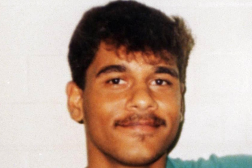 Headshot of a young man with a moustache wearing prison greens.