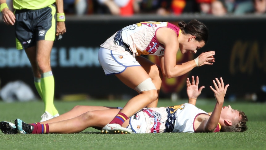 Brisbane players, one crouching over another lying on the ground, celebrate