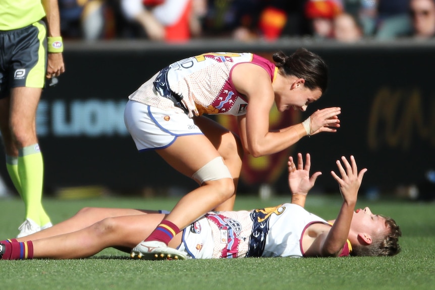 Brisbane players, one crouching over another lying on the ground, celebrate