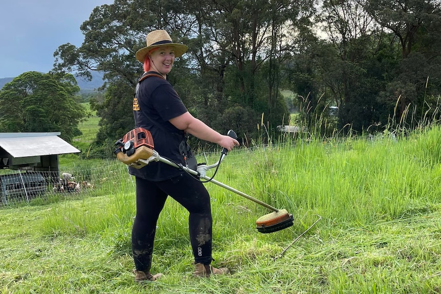 A woman in a paddock whipper snipping.