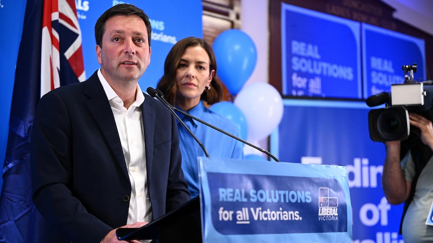 Victorian Opposition leader Matthew Guy stands at a podium next to his wife, who's wearing blue.