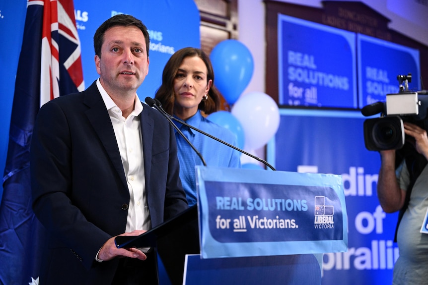 Victorian Opposition leader Matthew Guy stands at a podium next to his wife, who's wearing blue.