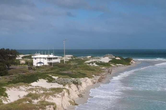 Two storey white building sits behind sand dunes at beach 