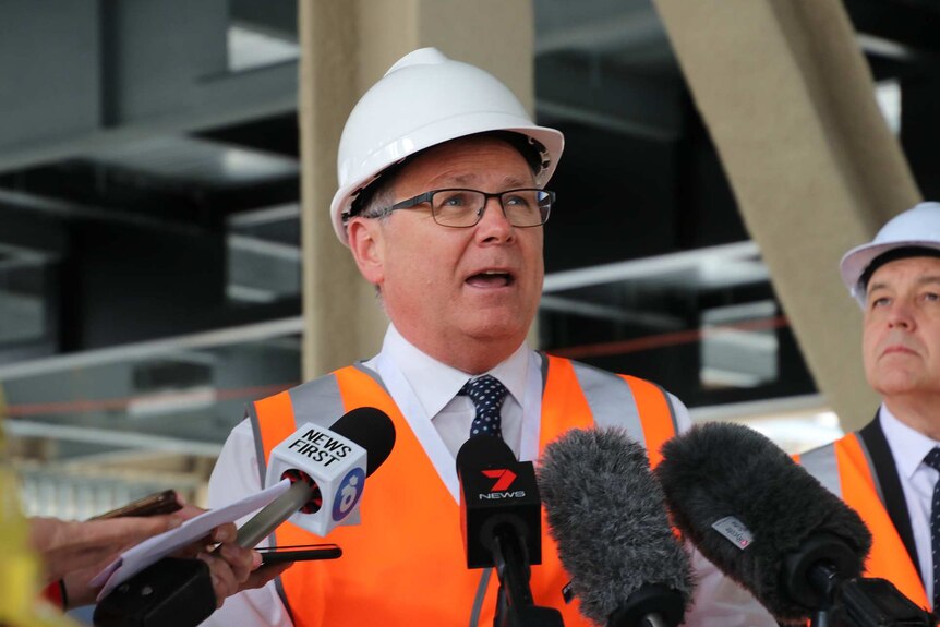 Minister David Templeman in high-vis vest at a press conference.