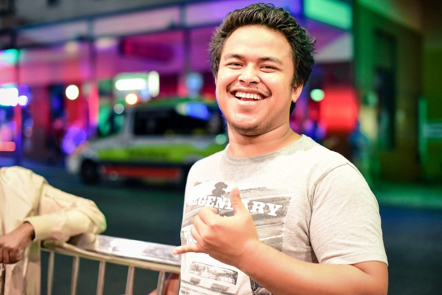 A man smiling and gesturing at the camera in Brisbane's Fortitude Valley.