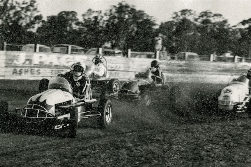 Four-wheel low-to-the-ground speed cars kick up the dust at a dirt circuit.