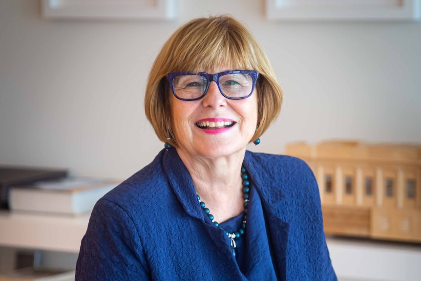 A woman with chin-length auburn hair with blue glasses and a blue suit  smiles