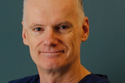 headshot of man in blue scrubs against plain green background.