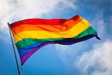 A rainbow coloured flag against the sky.
