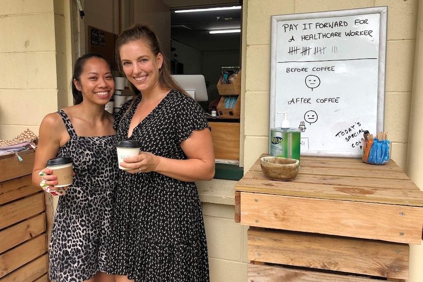 Two women smiling and holding takeaway coffees outside a cafe