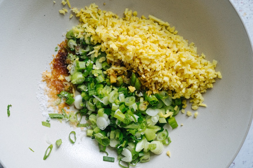 Finely chopped spring onions, ginger and soy sauce assembled in a bowl. 
