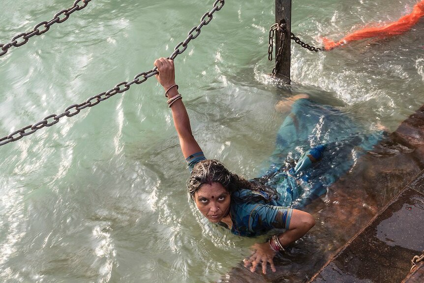 A woman looks up at the camera while bathing in the river.