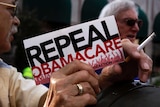 A man's hand holds a small sign reading "Repeal Obamacare" at a demonstration in Indiana 2013.