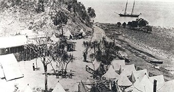 A black and white photo of a tented camp by the beach.