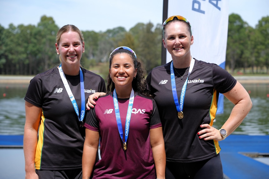 Three female paracanoe athletes stand next to each other smiling, with medals around their necks