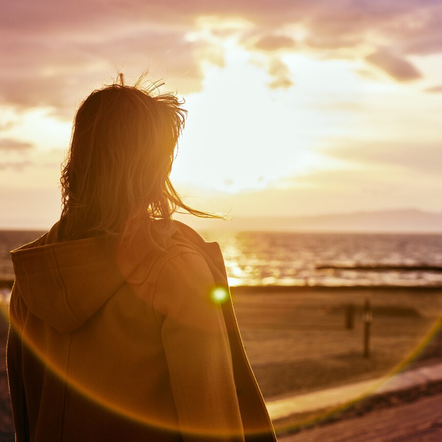 a woman looks out at the ocean as the sun sets on the horizon