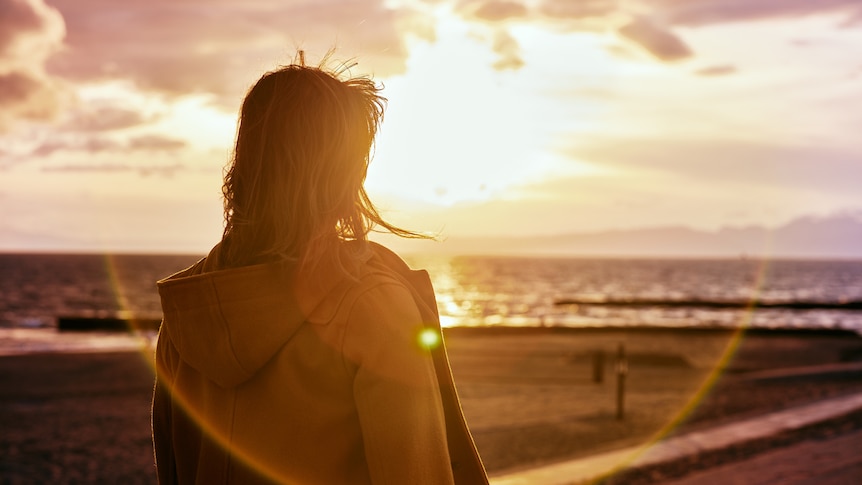a woman looks out at the ocean as the sun sets on the horizon