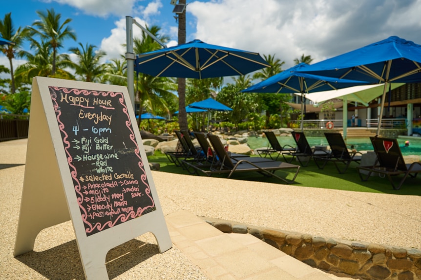 An a-frame chalk board advertises HAPPY HOUR Everyday 4pm - 6pm, listing beers, wines and selected cocktails